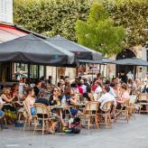 Des gens sont assis à des tables en terrasse dans une place animée à Vincennes.