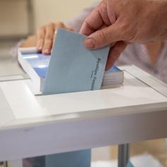 Vue de la main d’un homme déposant son bulletin de vote dans l’urne