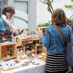 Une femme tenant un stand de bijoux rit avec des clientes