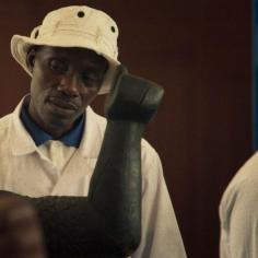 On voit un homme avec un bob blanc qui regarde une statue en bois