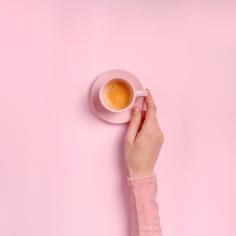 La main de la femme tenant une tasse de café sur fond rose
