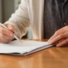 Les mains d’un homme de pension lisent des documents de retraite sur la police, les options de placement et la couverture funéraire tout en planifiant les finances, les assurances et le budget à la maison