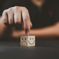 L’homme pointe la main sur un cube en bois avec un sourire heureux face du côté lumineux et un visage malheureux sur le côté sombre du cube de bloc de bois pour une sélection d’état d’esprit positif.