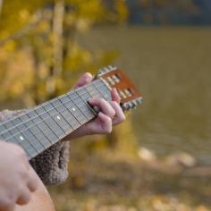 Gros plan des mains de l’artiste joue de la guitare acoustique en bois dans le parc d’automne. 