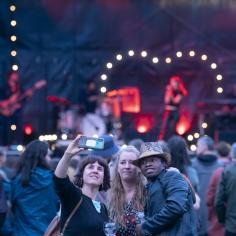 On voit trois personnes qui prennent une photo et dans le fond on aperçoit une scène de concert