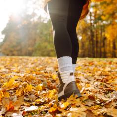 Gros plan des jambes d’une jeune randonneuse en chaussures de randonnée marchant sur des feuilles mortes brillantes.