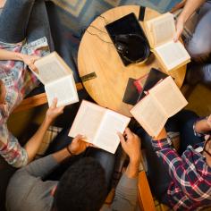 Groupe diversifié d’amis discutant d’un livre en bibliothèque.