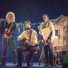 Trois artistes sont sur une scène et sourient à la caméra