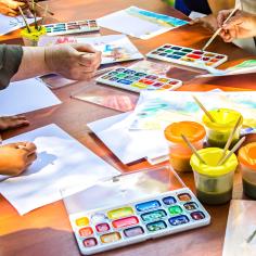 Plusieurs personnes dessinent sur du papier à l’aide de peintures à l’aquarelle assises à la même table