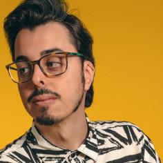 Un homme brun avec des lunettes regarde à droite et le fond est jaune-orangé