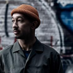 un homme pose devant un mur de graffiti et porte un petit bonnet orange