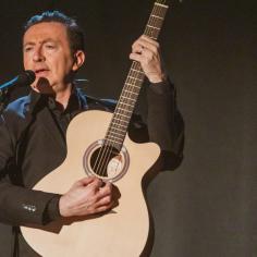 Un homme sur scène avec une guitare devant un micro