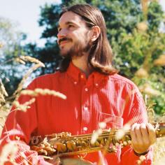 Un homme au cheveu long tient un saxophone dans la ses mains