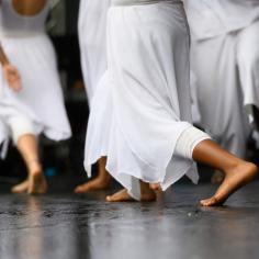 Des danseuses en robes blanches fluides se produisent pieds nus sur scène lors d’une danse contemporaine gracieuse