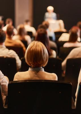 on y voit des personnes de dos qui écoutent un orateur