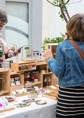 Une femme tenant un stand de bijoux rit avec des clientes