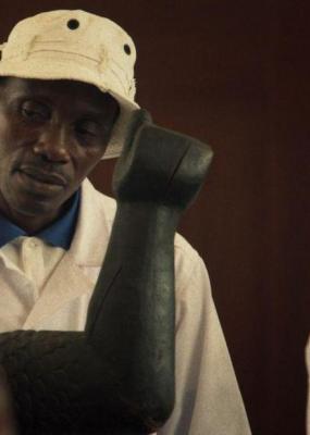 On voit un homme avec un bob blanc qui regarde une statue en bois