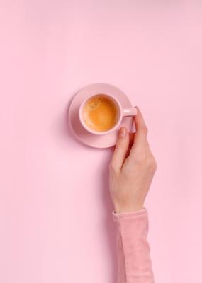 La main de la femme tenant une tasse de café sur fond rose