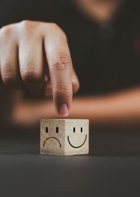L’homme pointe la main sur un cube en bois avec un sourire heureux face du côté lumineux et un visage malheureux sur le côté sombre du cube de bloc de bois pour une sélection d’état d’esprit positif.