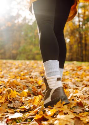 Gros plan des jambes d’une jeune randonneuse en chaussures de randonnée marchant sur des feuilles mortes brillantes.
