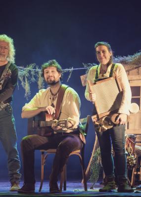 Trois artistes sont sur une scène et sourient à la caméra