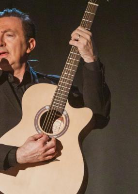 Un homme sur scène avec une guitare devant un micro