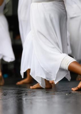 Des danseuses en robes blanches fluides se produisent pieds nus sur scène lors d’une danse contemporaine gracieuse