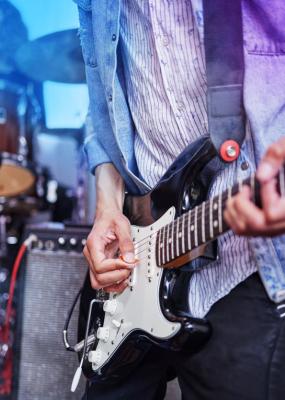 Plan recadré d’un guitariste méconnaissable jouant sur scène avec ses camarades de groupe en arrière-plan 