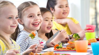 Un groupe d'enfants souriants mange des repas dans une salle de restauration.
