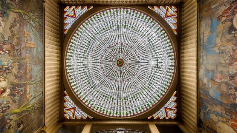 Vue plongeante de la grande coupole vitrée de l'Hôtel de Ville de Vincennes, encadrée par des fresques murales.
