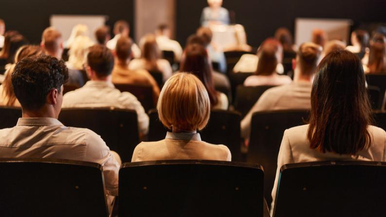 on y voit des personnes de dos qui écoutent un orateur