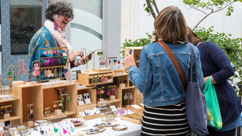 Une femme tenant un stand de bijoux rit avec des clientes