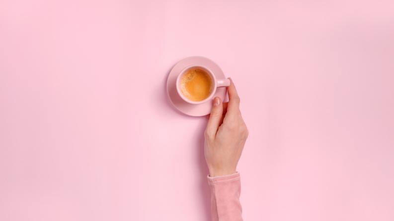 La main de la femme tenant une tasse de café sur fond rose