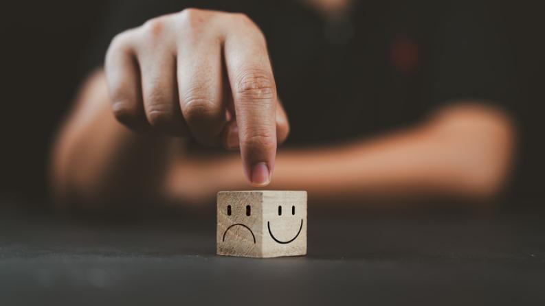 L’homme pointe la main sur un cube en bois avec un sourire heureux face du côté lumineux et un visage malheureux sur le côté sombre du cube de bloc de bois pour une sélection d’état d’esprit positif.