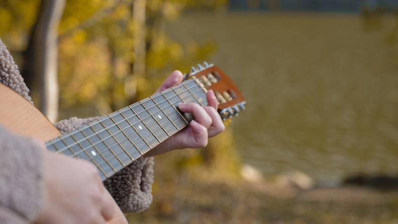 Gros plan des mains de l’artiste joue de la guitare acoustique en bois dans le parc d’automne. 