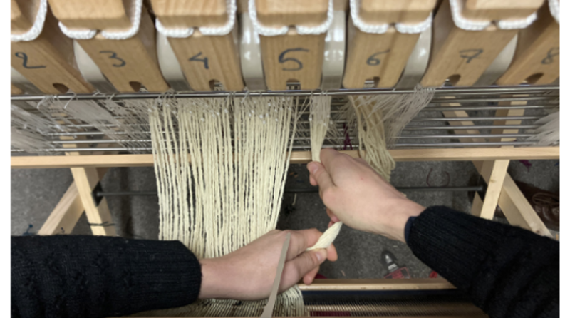 des personnes tiennent de la laine sur une machine à tisser