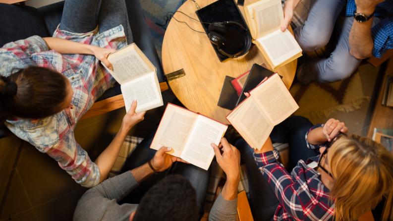 Groupe diversifié d’amis discutant d’un livre en bibliothèque.