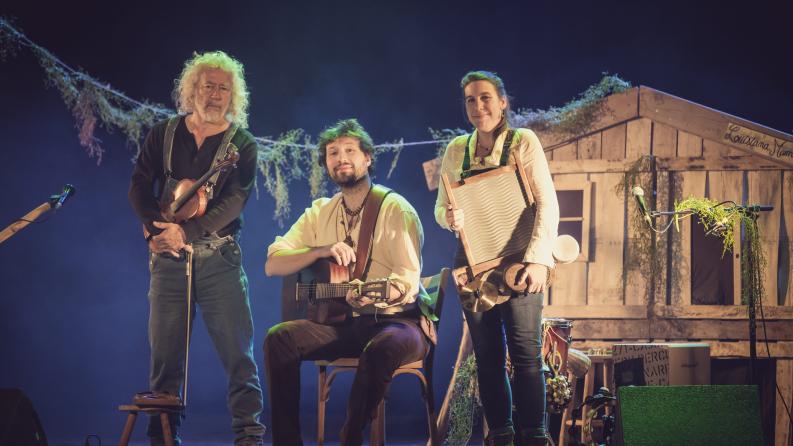 Trois artistes sont sur une scène et sourient à la caméra