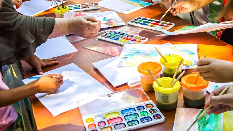 Plusieurs personnes dessinent sur du papier à l’aide de peintures à l’aquarelle assises à la même table