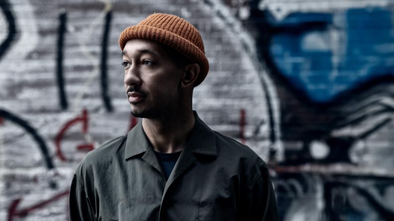 un homme pose devant un mur de graffiti et porte un petit bonnet orange