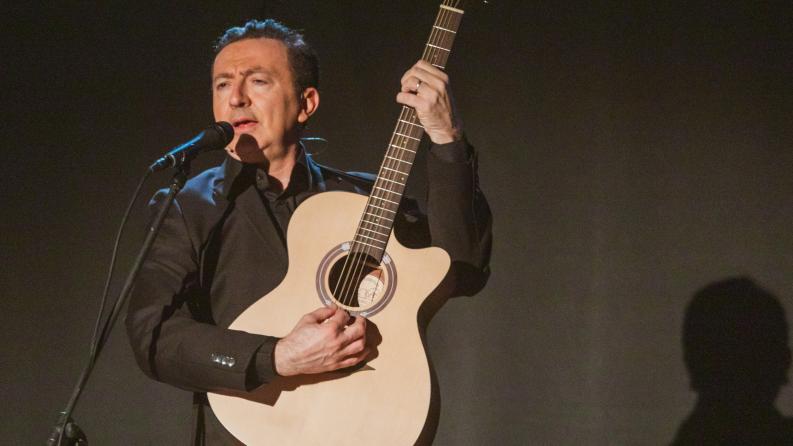 Un homme sur scène avec une guitare devant un micro