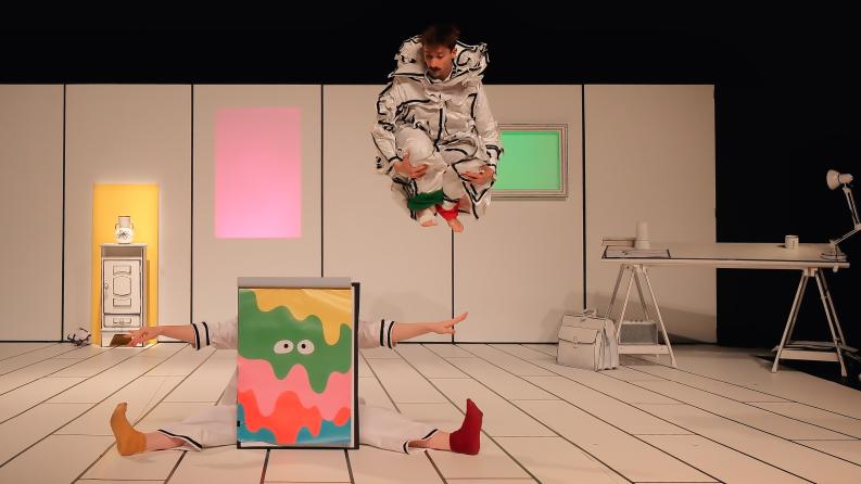 Deux danseurs déguisés sur scène, l'un saute et l'autre est assis