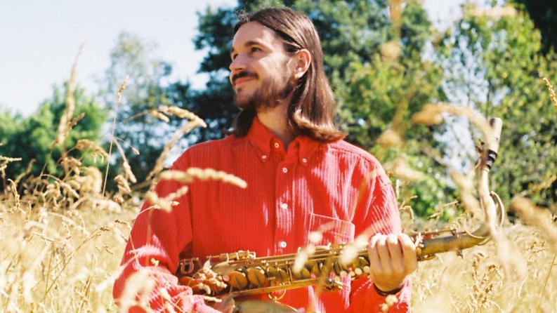 Un homme au cheveu long tient un saxophone dans la ses mains