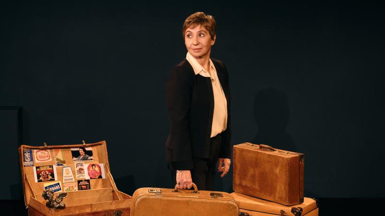 une femme sur scène se tient debout à côté de plusieurs valises anciennes