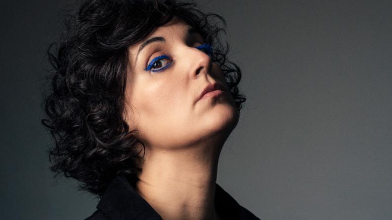 Une femme brune regarde la caméra et porte un eye liner bleu électrique