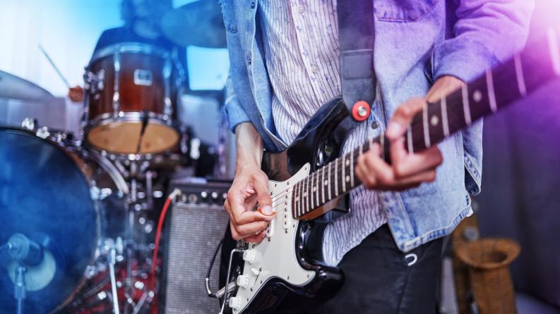 Plan recadré d’un guitariste méconnaissable jouant sur scène avec ses camarades de groupe en arrière-plan 