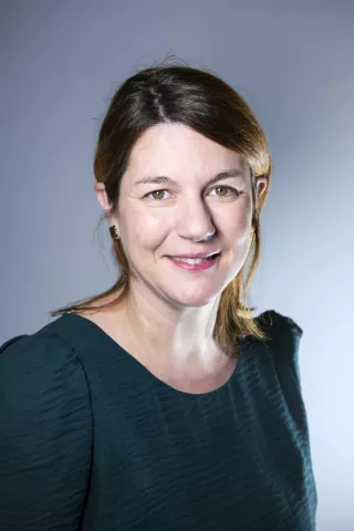 Une femme portant un haut vert sourit à l'écran