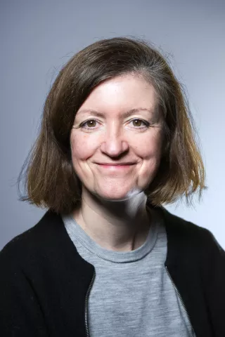 Une femme brune portant un gilet noir regarde l'objectif en souriant