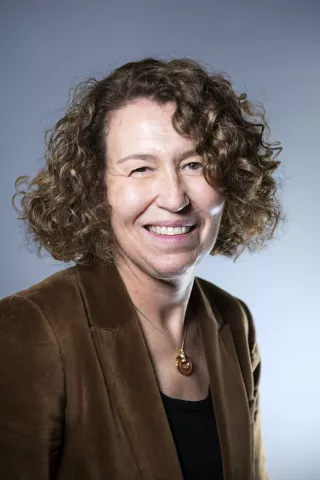 Une femme brune aux cheveux bouclés sourit à l'écran