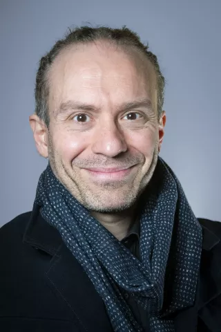 Un homme brun qui porte une écharpe sourit à l'objectiff